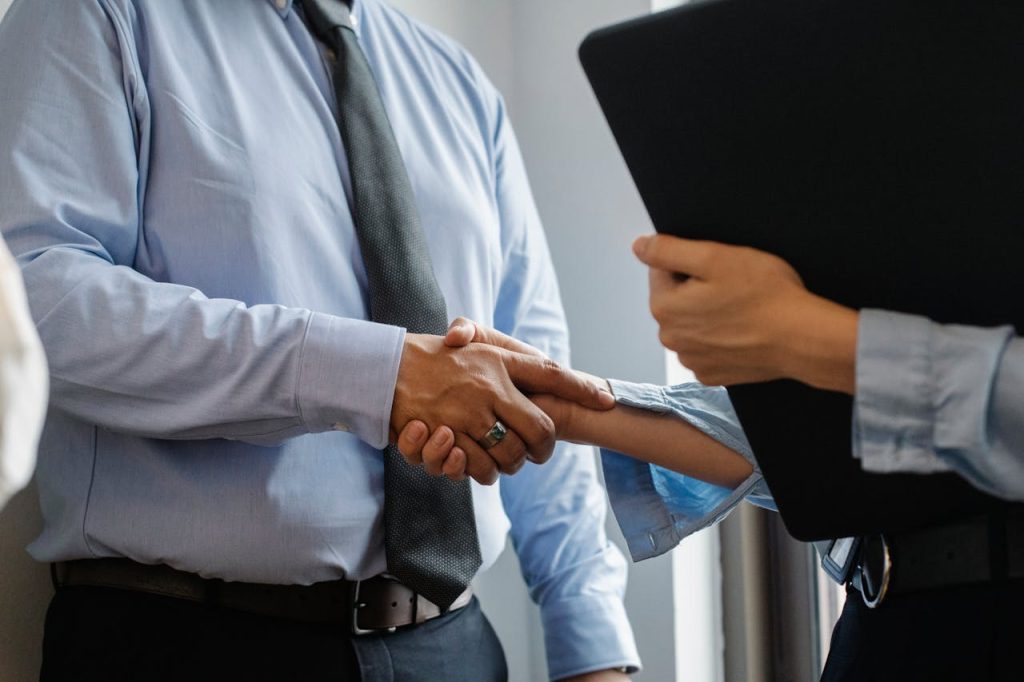 man-and-woman-shaking-hands-in-office-5668842 Crop anonymous man in formal shirt and tie shaking hand of woman with black folder while meeting in office