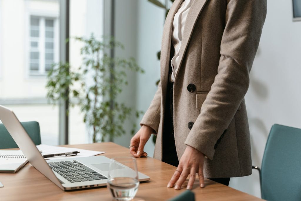 person-in-brown-coat-holding-clear-drinking-glass-7223036 A professional businesswoman in a stylish office environment with a laptop and notes.
